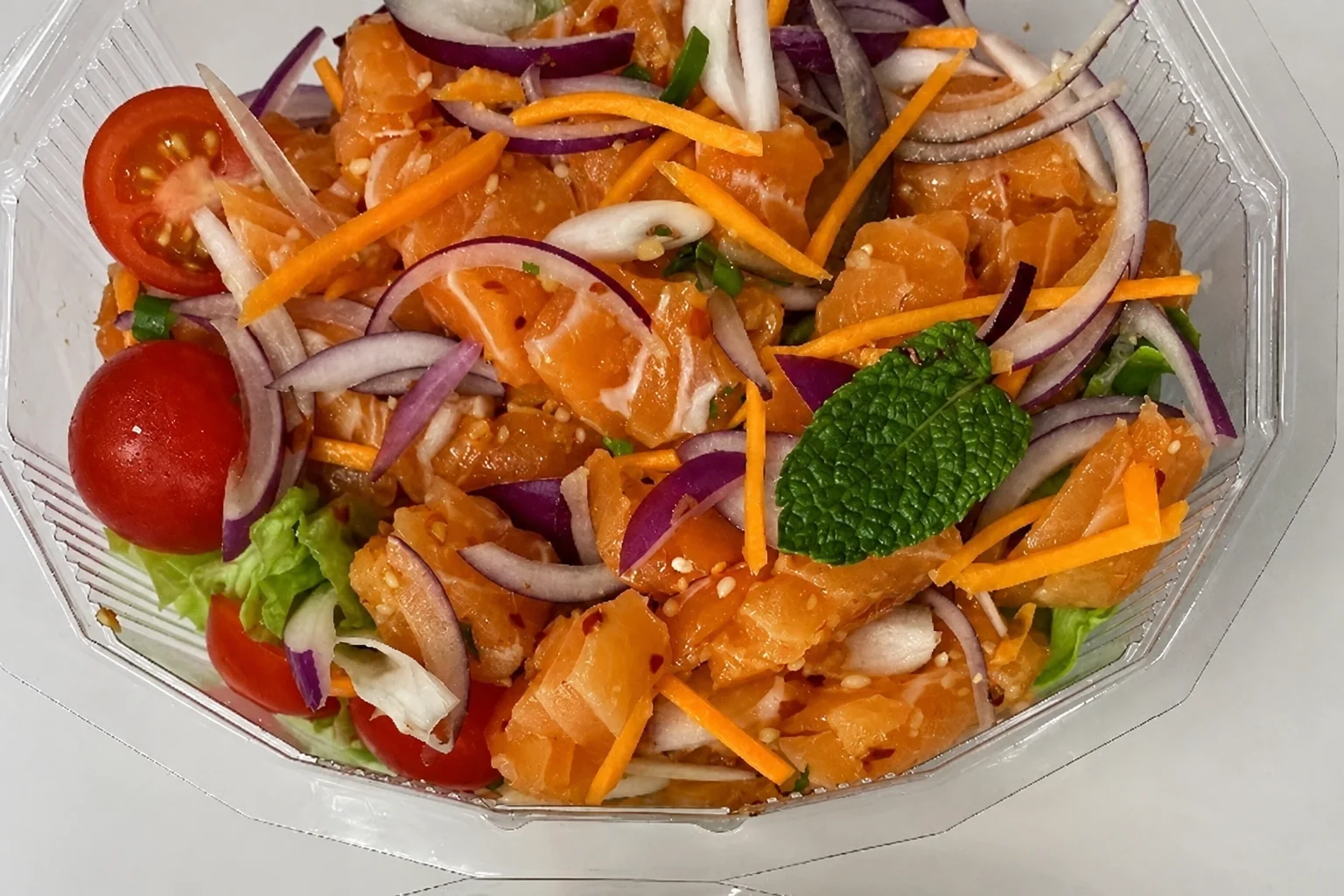 Salmon salad with lemongrass in a transparent box on a pale background